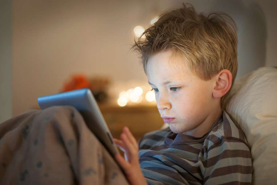 boy sitting up in bed with electronic tablet